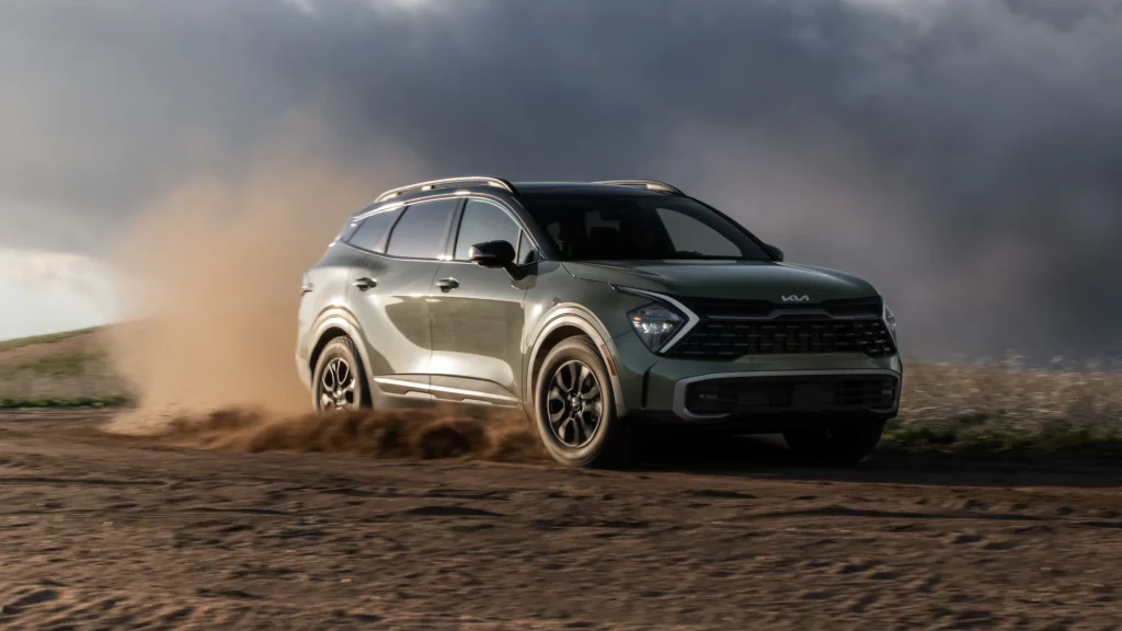 2025 Kia Sportage in green, driving off-road on dirt terrain with dust trail against a cloudy sky backdrop.