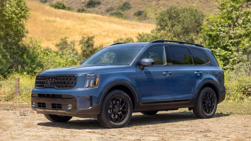 2025 Kia Telluride in blue, front-side exterior view, black alloy wheels, parked outdoors on dirt road.