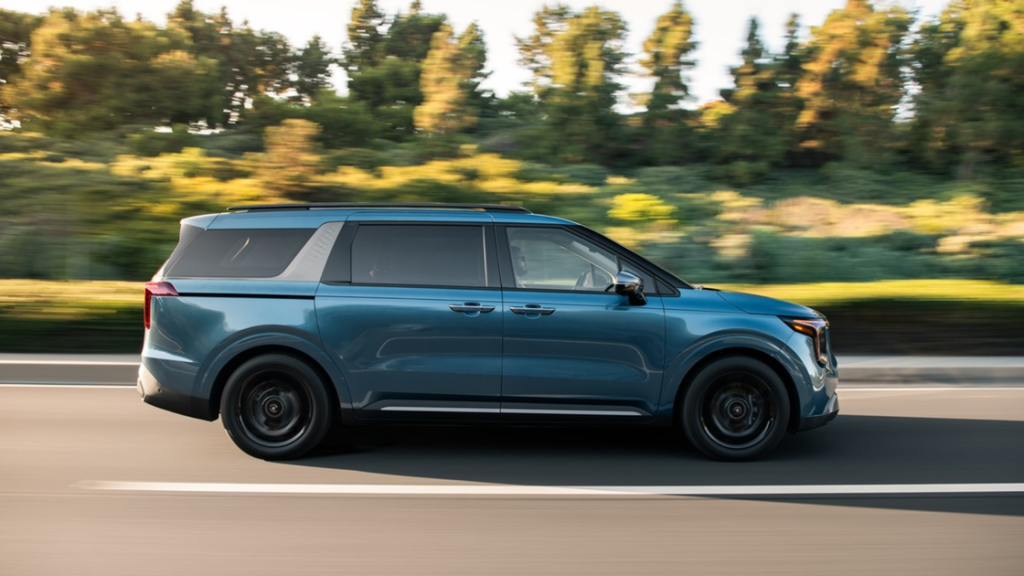 2026 Kia Carnival minivan in motion, blue exterior, side profile view on city road.