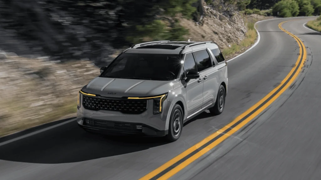 2026 Kia Carnival HEV in motion on a winding road showcasing modern hybrid minivan design.