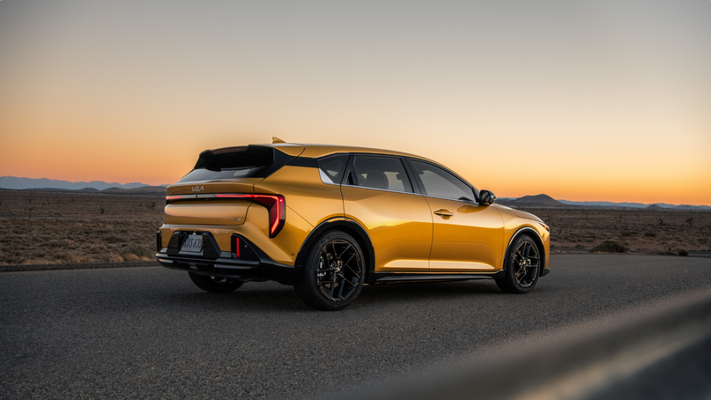 2026 Kia K4 Hatchback rear three quarter view in gold finish driving on open desert road at sunset.