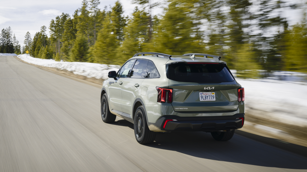 2026 Kia Sorento rear three quarter view in green driving on snowy mountain road with roof rails.
