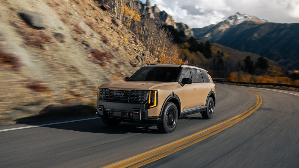 2027 Kia Telluride front three quarter view in tan driving through mountain canyon road.