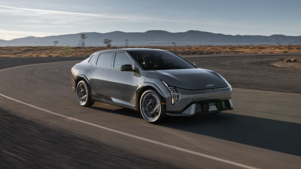 2026 Kia EV4 electric sedan driving on a desert road, front three-quarter exterior view in gray.