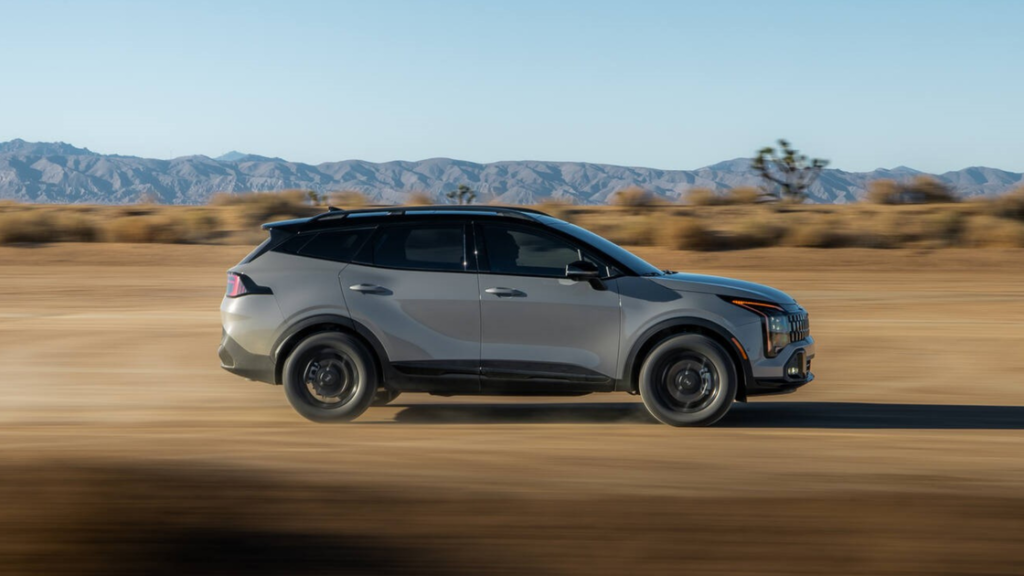 2026 Kia Sportage SUV side profile driving on an open desert highway with mountains in background.