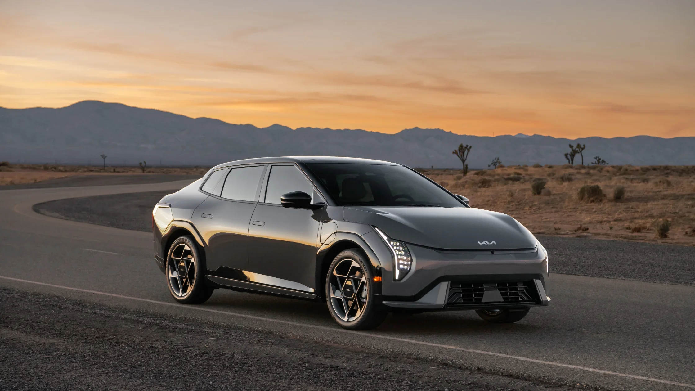 2026 Kia EV4 gray exterior parked on desert road at sunset with LED headlights on.