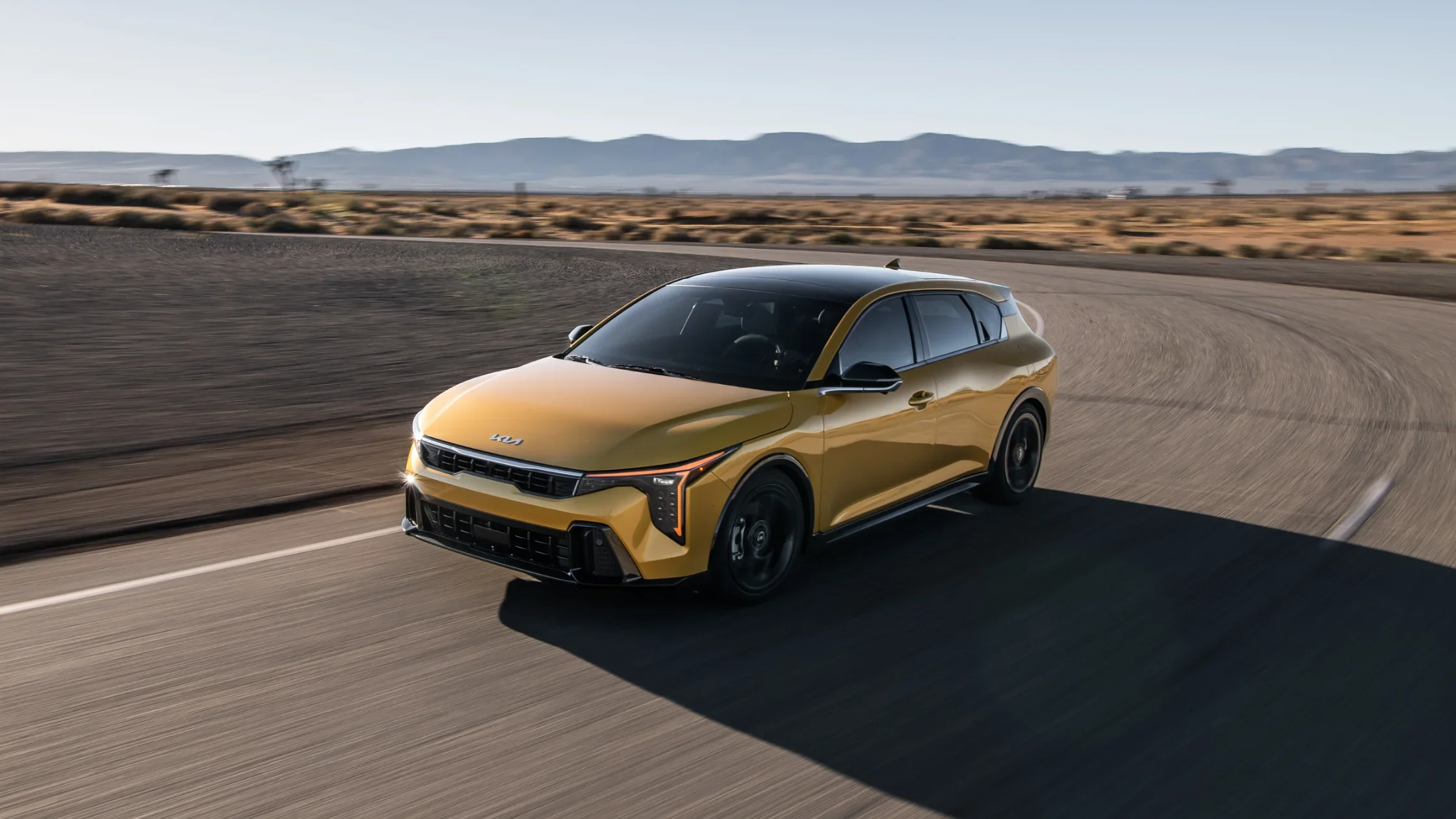 2026 Kia K4 Hatchback in yellow driving on desert highway with black roof and sharp LED headlights.