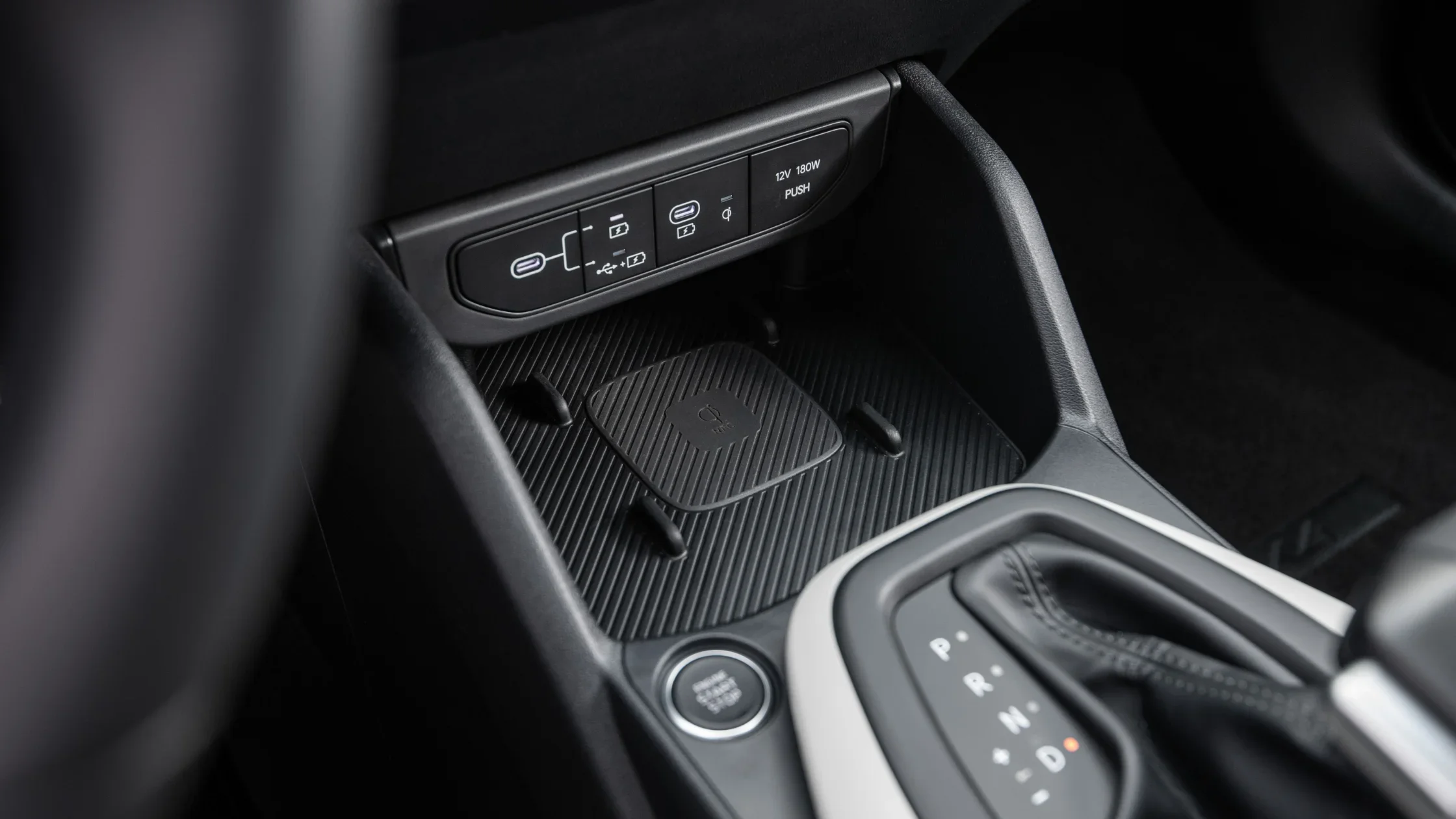 Close-up of 2025 Kia K4’s center console with wireless charging pad, USB ports, and push-start button.