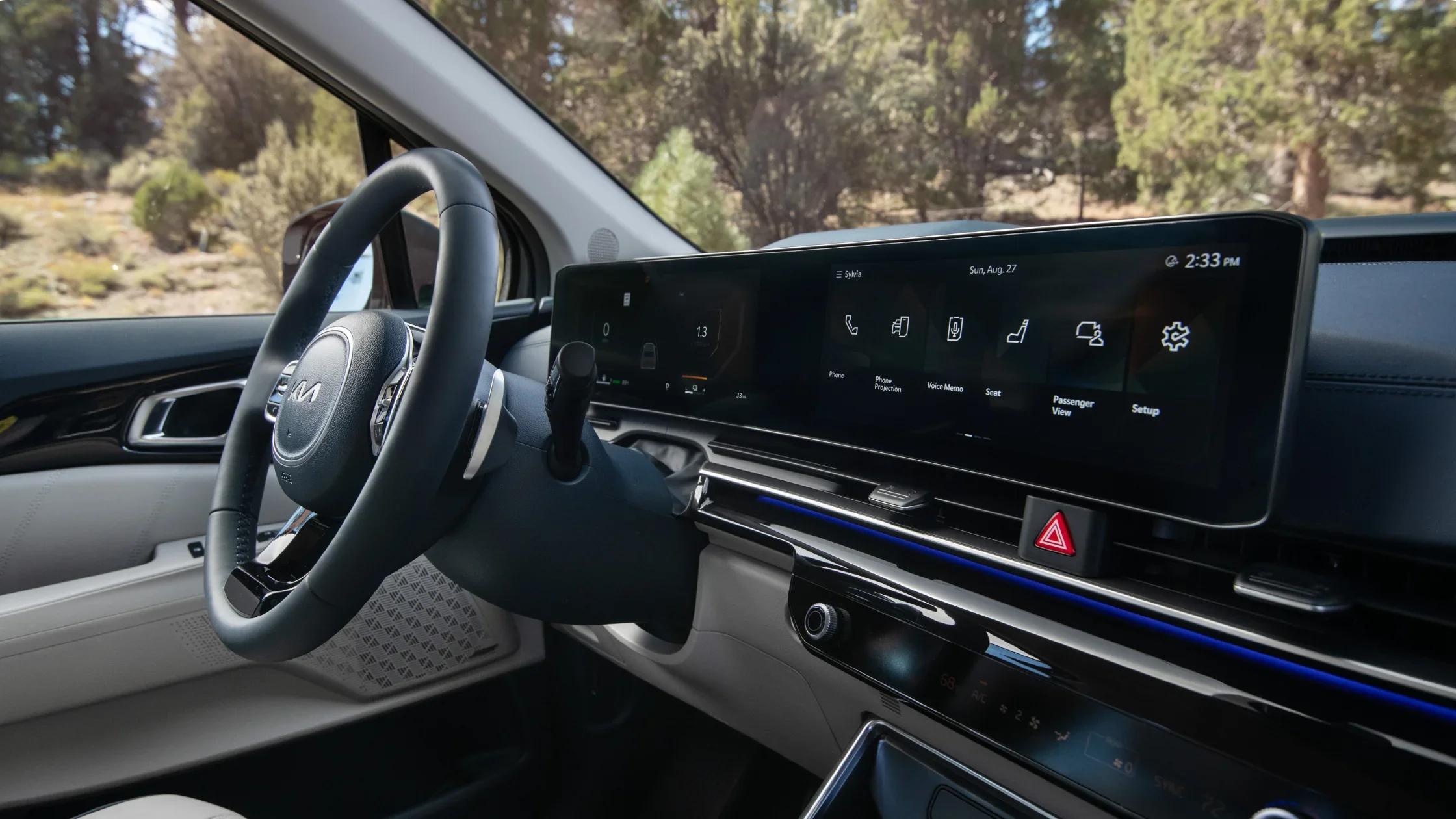Dashboard view of the 2025 Kia Carnival Hybrid with a wide digital display and forest backdrop.