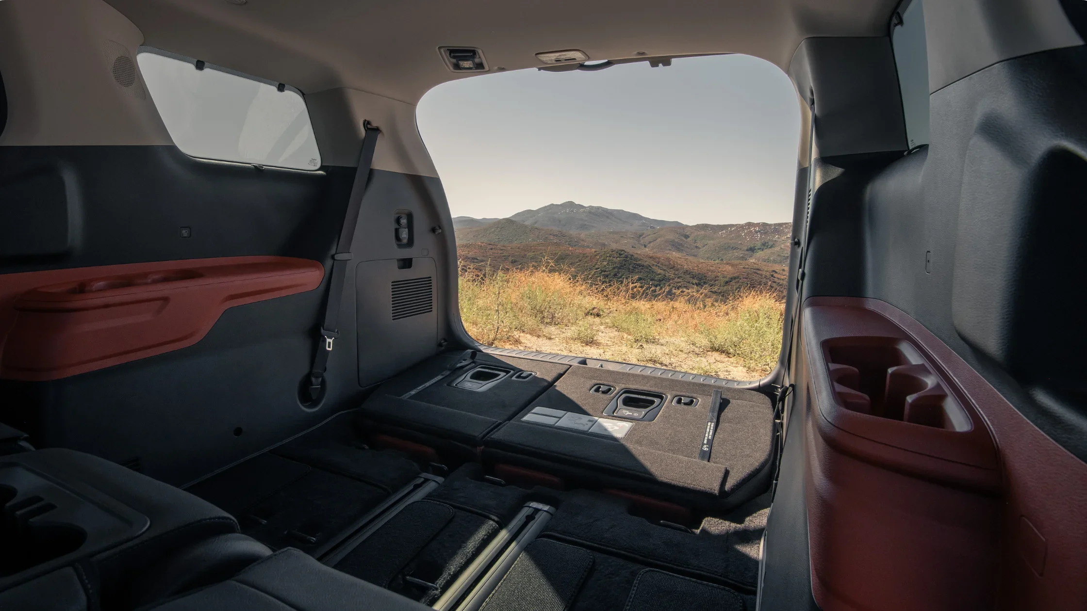 Rear cargo view of the 2025 Kia Carnival with seats folded flat and scenic mountains in the distance.