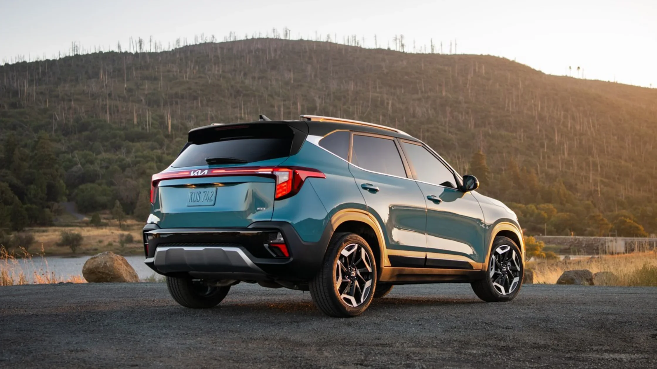 Teal 2026 Kia Seltos parked near a lake at sunset, highlighting its bold rear design and LED lighting.