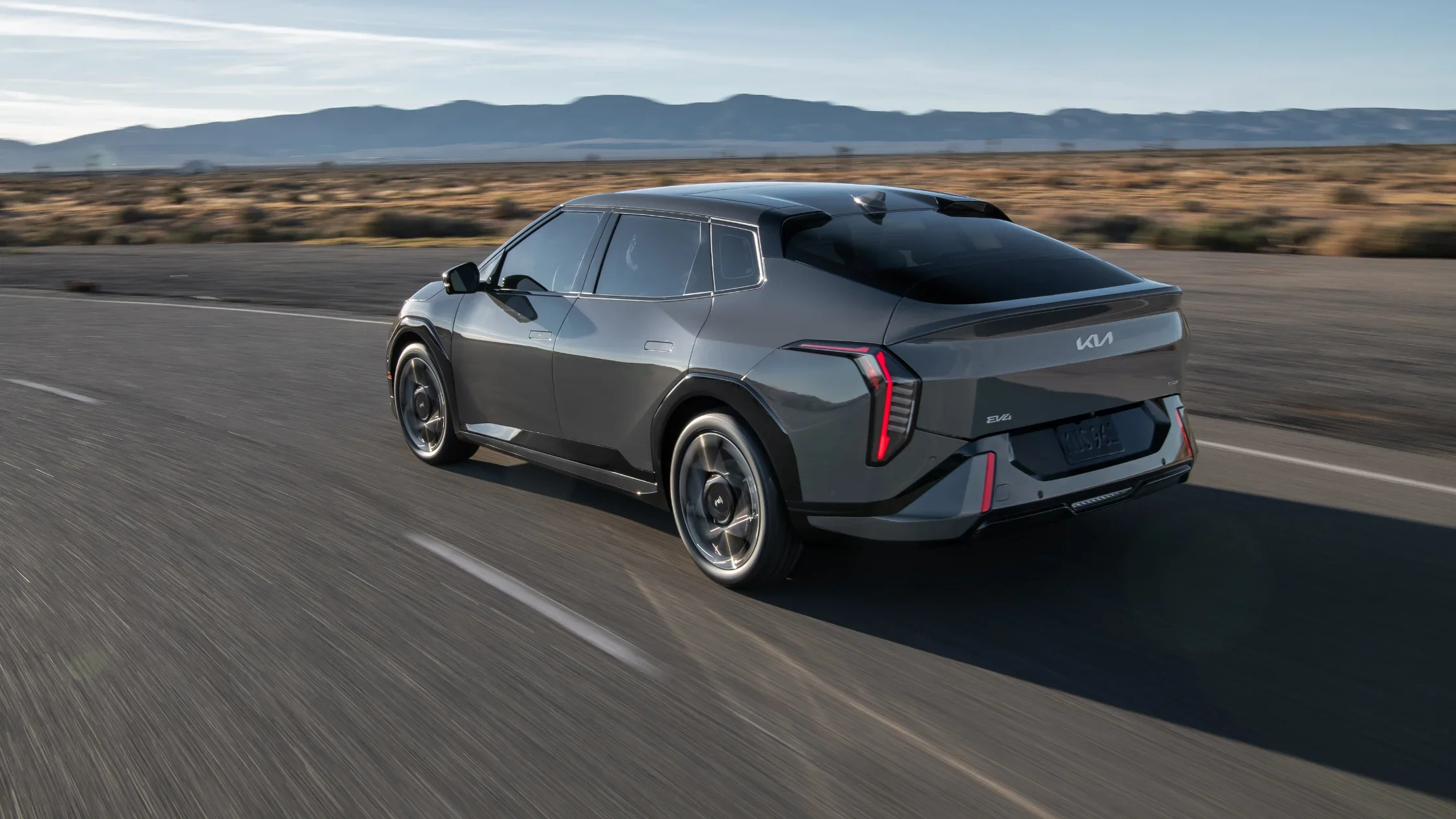 2026 Kia EV4 exterior rear three-quarter view driving along desert road with mountains.